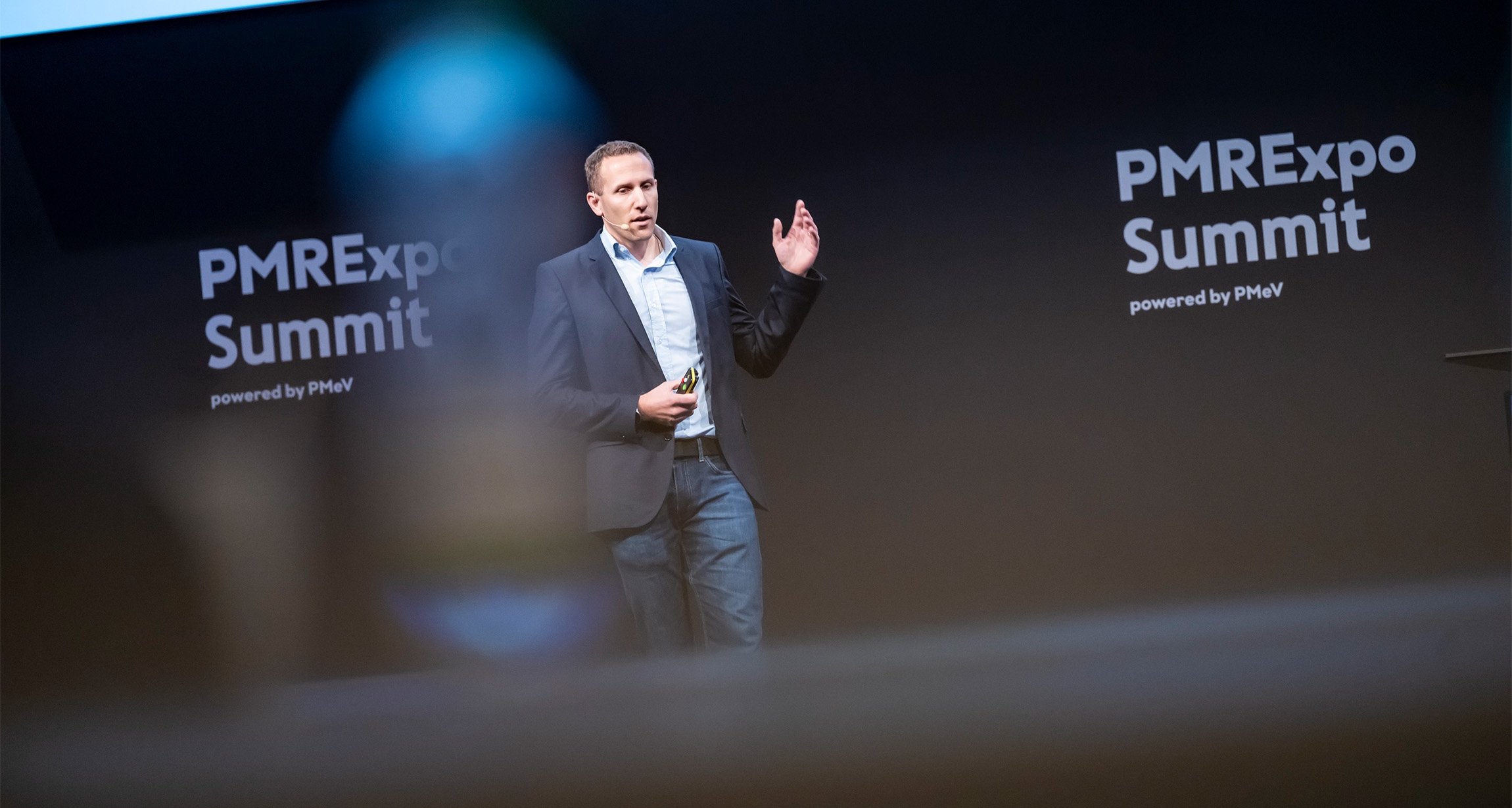 Ein Redner gestikuliert während seiner Präsentation auf dem PMRExpo-Gipfel, vor einem Hintergrund, der den Namen der Veranstaltung zeigt.