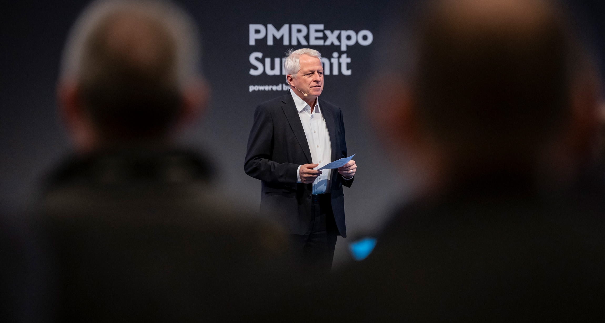 Ein Sprecher hält einen Vortrag auf dem PMRExpo-Gipfel, während die Zuhörer im Vordergrund teilweise zu sehen sind und gespannt zuhören.