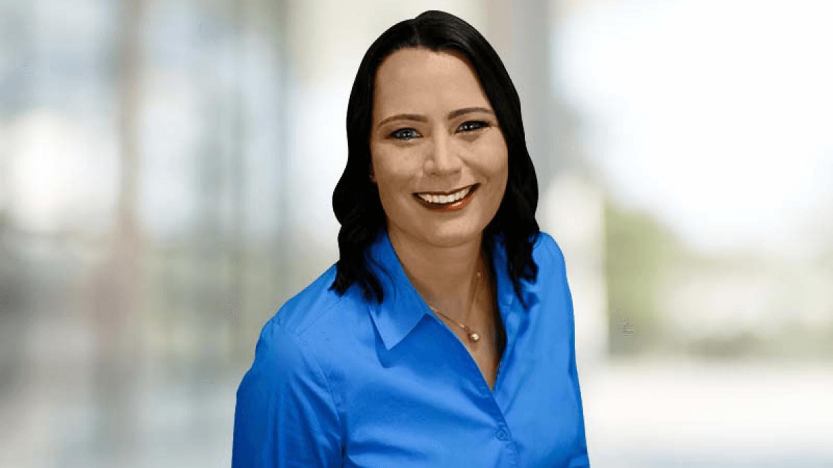 Eine lächelnde Frau mit schulterlangem, dunklem Haar trägt ein blaues Hemd und steht vor einem verschwommenen Hintergrund, während sie die neuesten Leitstellenlösungen von Omnitronics auf der PMRExpo in Köln präsentiert.