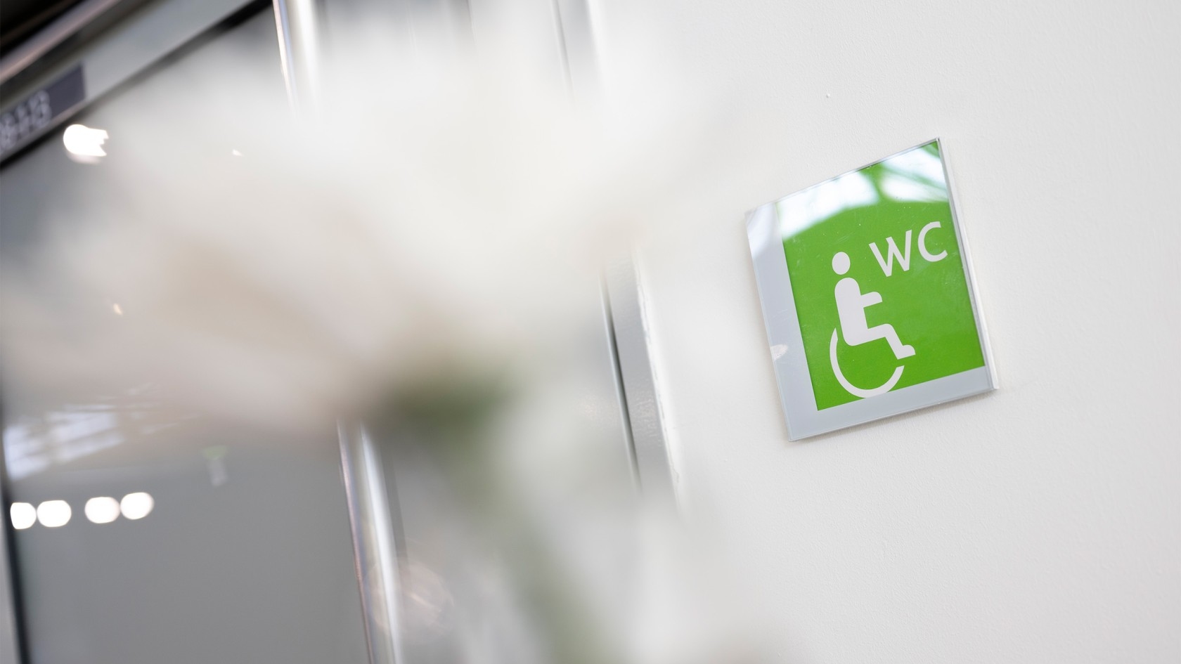 Green sign with white wheelchair symbol and letters 'WC' on a white wall.