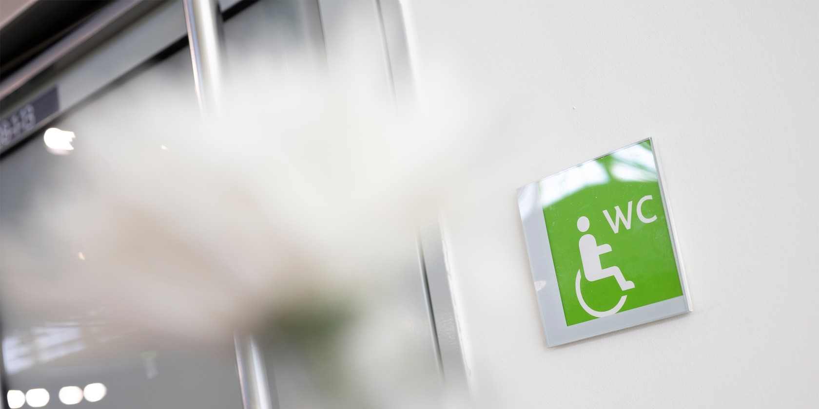 Green sign with white wheelchair symbol and letters 'WC' on a white wall.